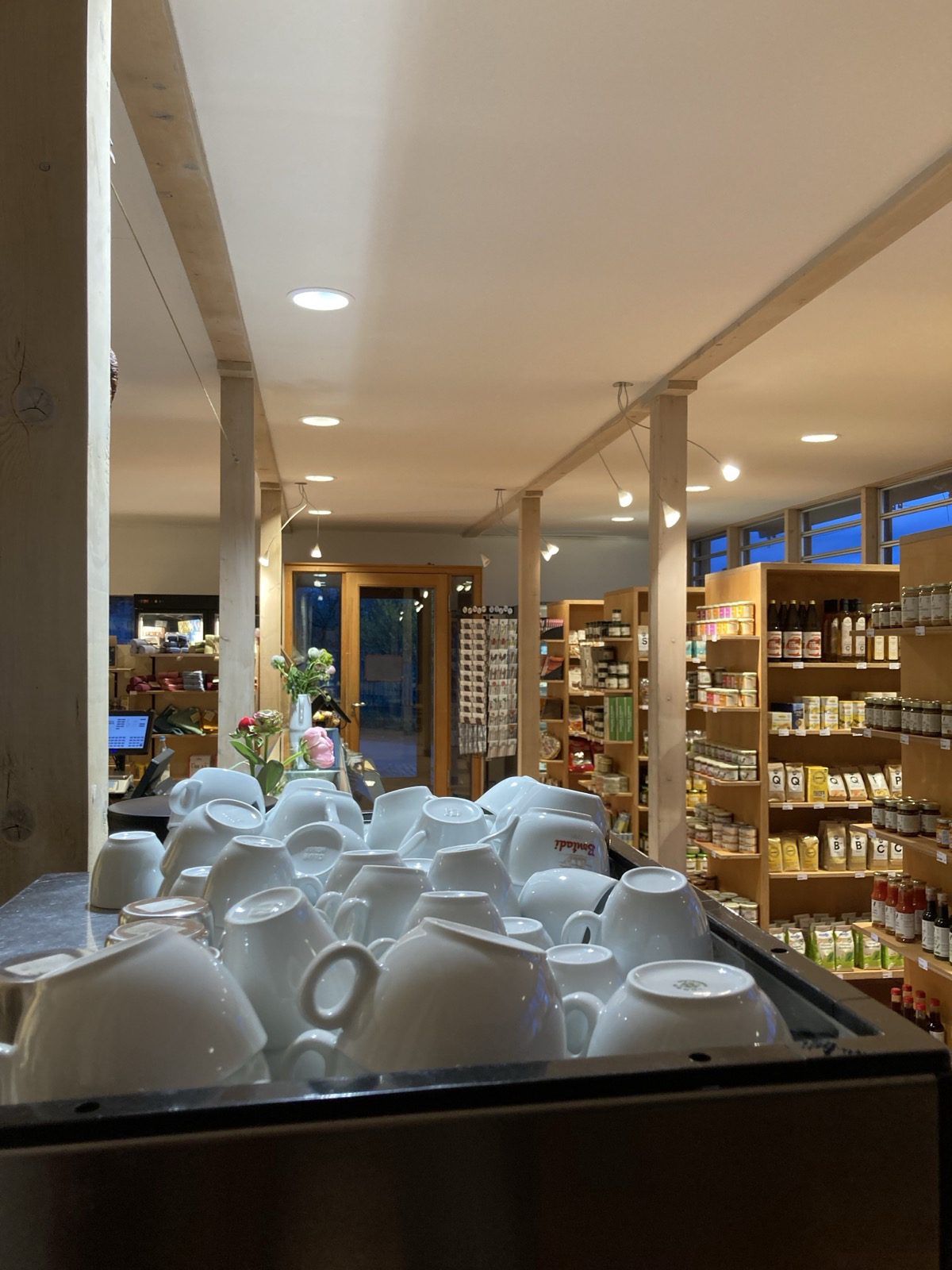 Blick vom Café-Tisch mit Blumen zur Käsetheke und zur La-Marzocco-Siebträgermaschine