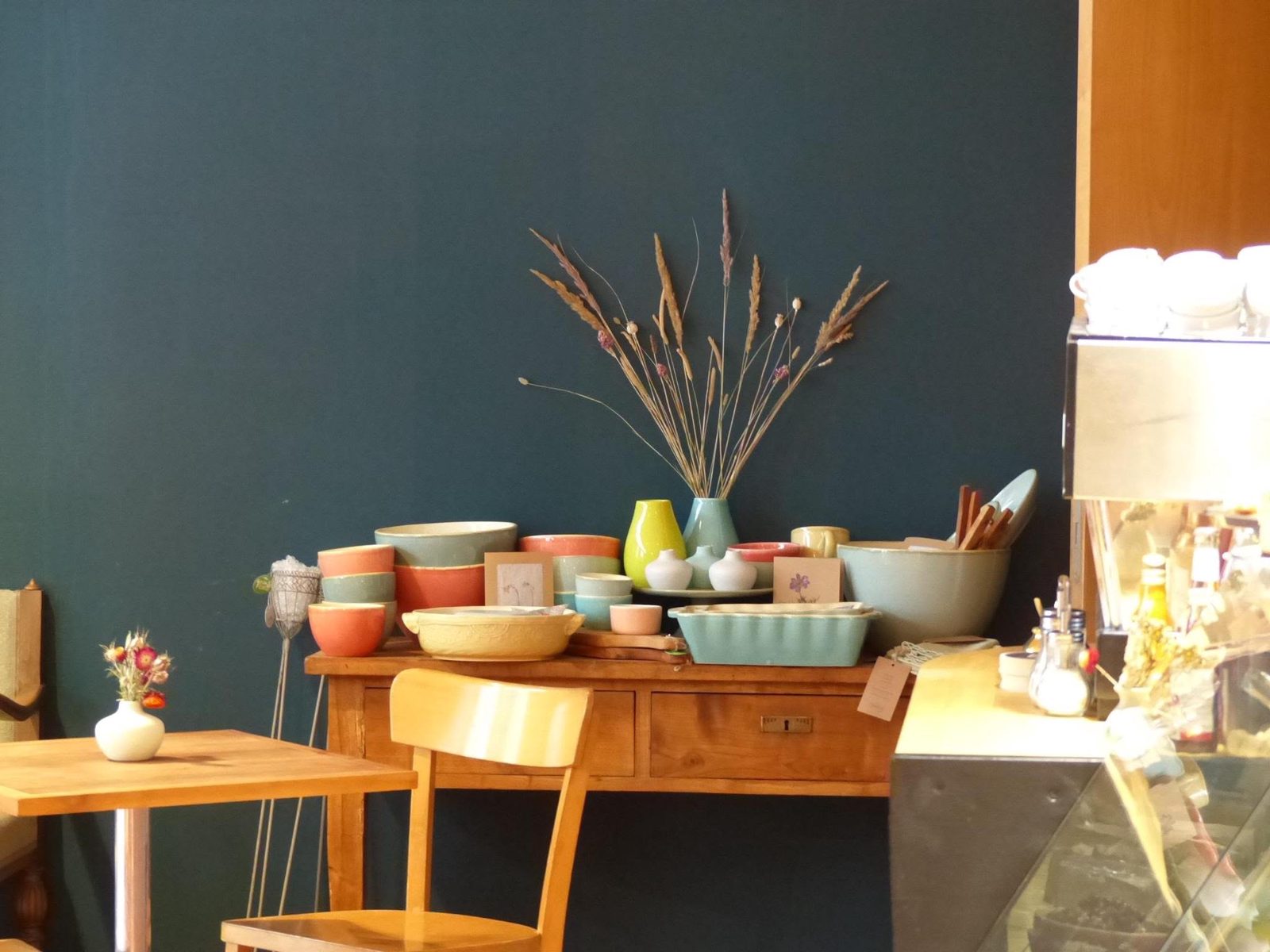 Bunte Keramikschüsseln und Trockengräser auf einem alten Holztisch vor der blauen Wand
