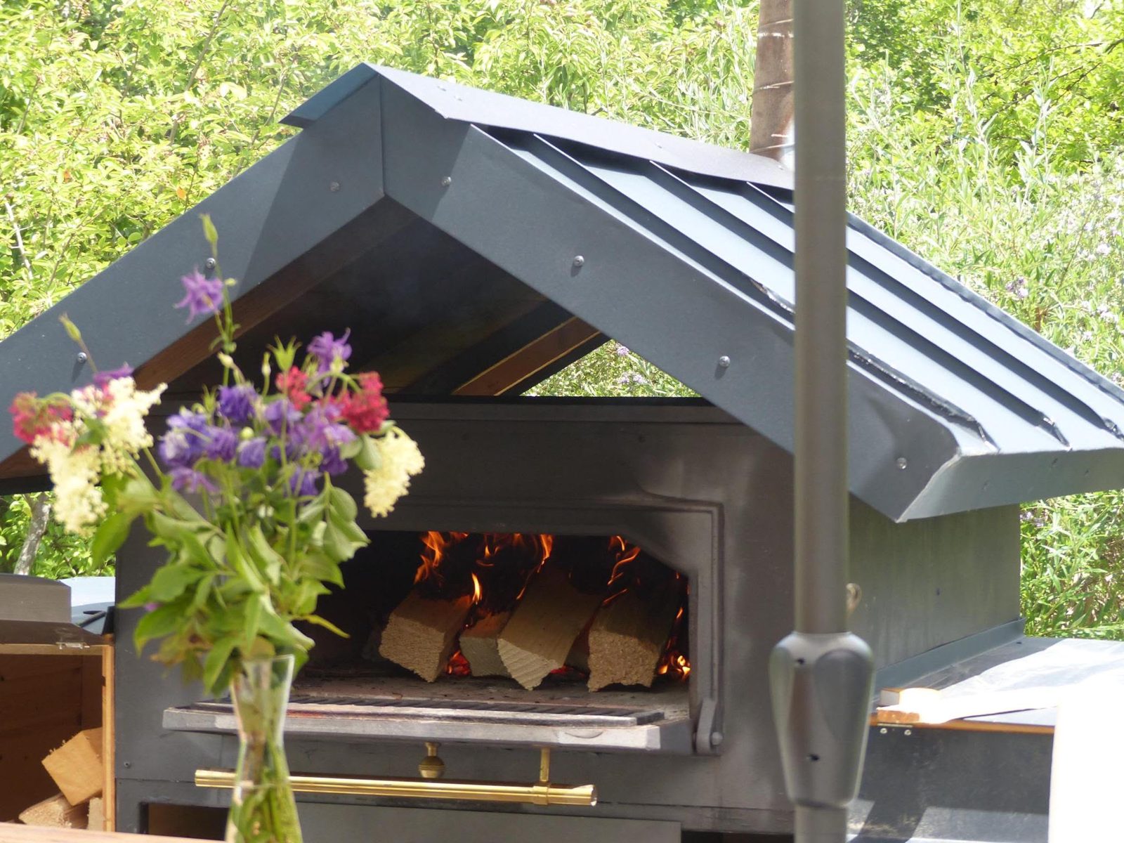 Der mobile Holzofen mit brennendem Feuer und einem Blumenstrauß im Vordergrund